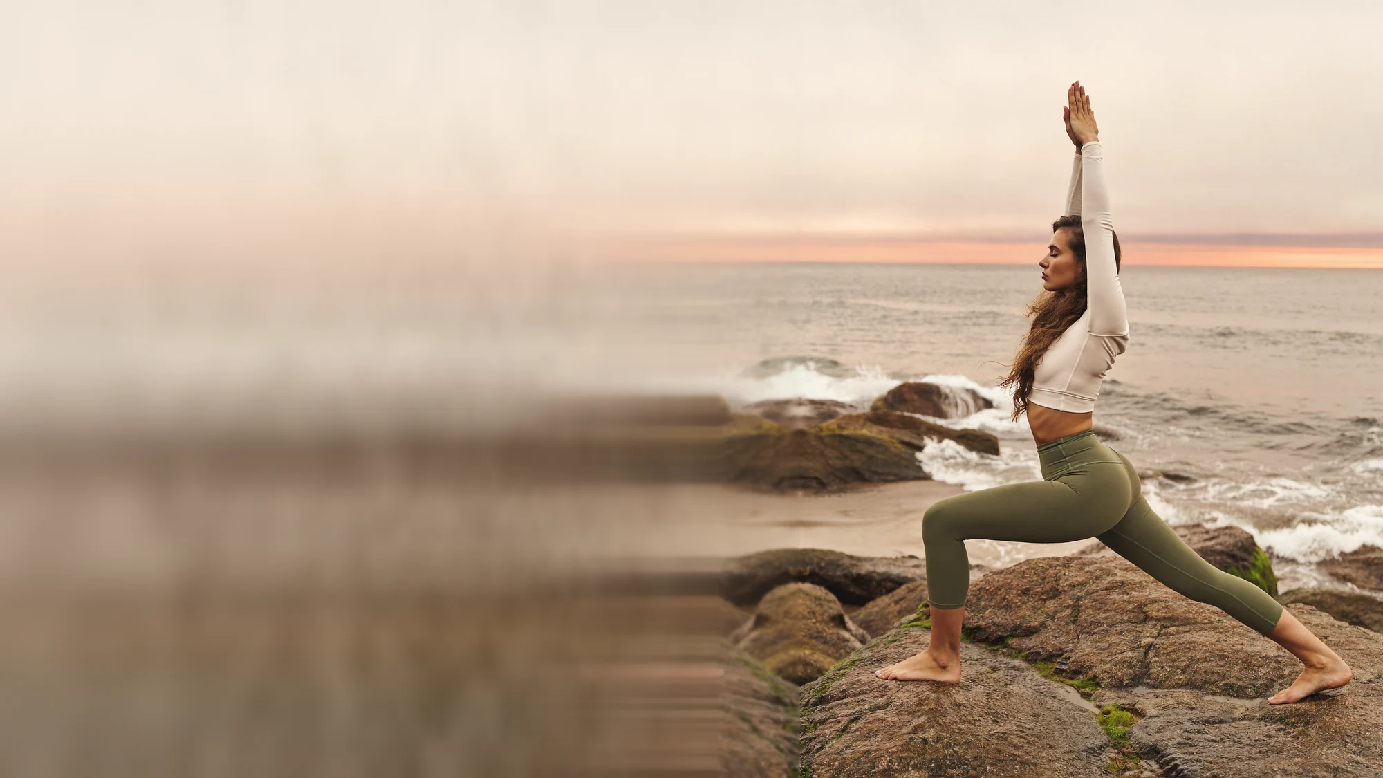 Woman in a high lunge on coastal rocks by the sea, arms raised